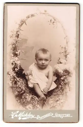 Fotografie H. Michler, Grottau, Portrait niedliches Kleinkind im weissen Hemd im Korbstuhl sitzend