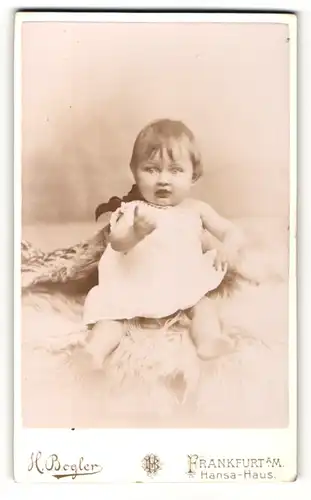 Fotografie H. Bogler, Frankfurt a. M., Baby im Taufkleid, auf einem Lammfell sitzend