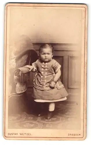 Fotografie Gustav Wetzel, Dresden, Portrait kleines Mädchen im hübschen Kleid an Stuhl gelehnt