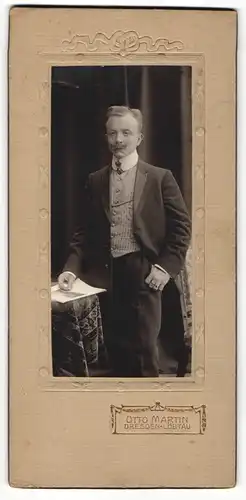 Fotografie Otto Martin, Dresden-Löbtau, Portrait elegant gekleideter Herr mit Zeitung an Tisch gelehnt