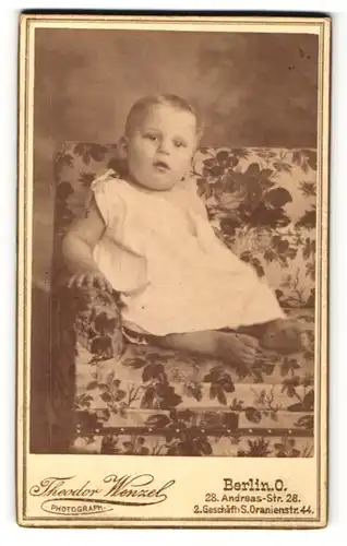 Fotografie Theodor Wenzel, Berlin-O, Portrait Kleinkind in Leibchen auf Sitzmöbel