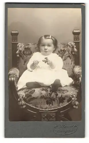Fotografie C. Klaucke, Torgau, Portrait kleines Mädchen im weissen Kleid mit Blume auf Stuhl sitzend