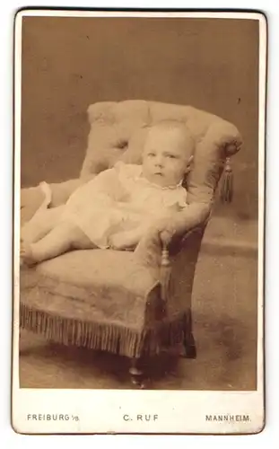 Fotografie C. Ruf, Freiburg i / B., Portrait niedliches Baby im weissen Hemd auf Sessel sitzend