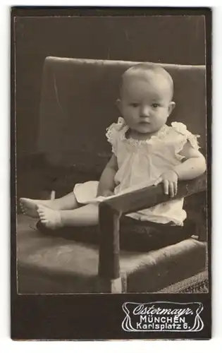 Fotografie Gebr. Ostermayr, München, Portrait süsses Kleinkind im weissen Kleidchen auf einem Stuhl