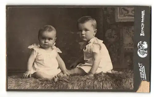 Fotografie Ebert, Bremen, Zwei Kleinkinder in weissen Laibchen auf Fellteppich