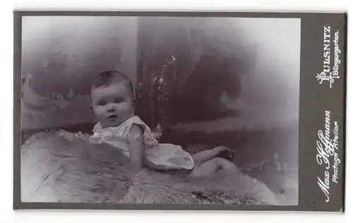 Fotografie Max Hoffmann, Pulsnitz, niedliches kleines Baby im weissen Hemdchen auf einem Lammfell