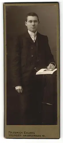 Fotografie Friedrich Ehlers, Solingen, junger Mann mit zurückgekämmtem Haar in Anzug mit Uhrenkette, Katalog vor sich