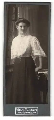Fotografie Wilh. Müller, Hof a / S., Portrait hübsch gekleidete Dame mit Buch an Tisch gelehnt