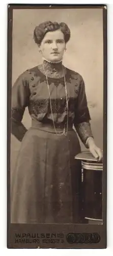 Fotografie W. Paulsen, Hamburg, Portrait hübsch gekleidete Dame mit Buch an Tisch gelehnt