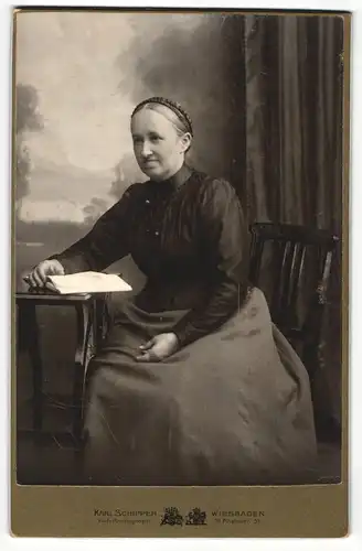 Fotografie Karl Schipper, Wiesbaden, Portrait bürgerlich gekleidete Dame mit Buch am Tisch sitzend