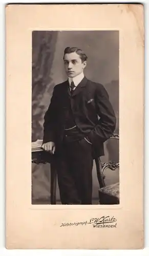 Fotografie L. W. Kurtz, Wiesbaden, Portrait elegant gekleideter Herr mit Zeitung an Tisch gelehnt