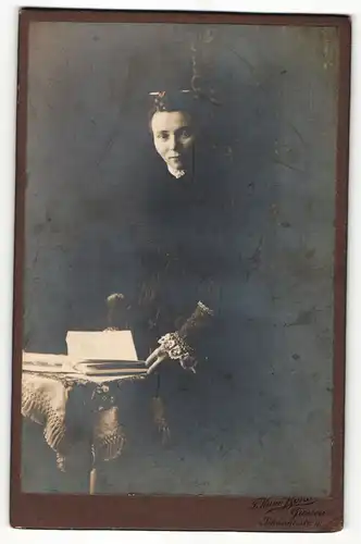 Fotografie T. Kuno Borst, Giessen, Portrait elegant gekleidete Dame mit Buch an Tisch gelehnt