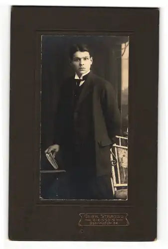 Fotografie Gebr. Strauss, Giessen, Portrait elegant gekleideter Herr mit Buch an Tisch gelehnt