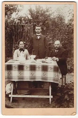 Fotografie unbekannter Fotograf und Ort, Portrait bürgerlich gekleidete Familie am Gartentisch sitzend