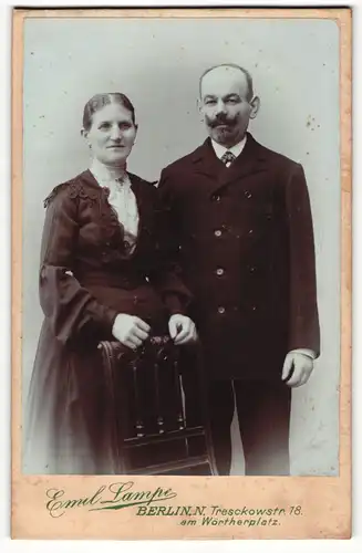 Fotografie Emil Lampe, Berlin-N, Portrait bürgerliches Paar in eleganter Kleidung an Stuhl gelehnt