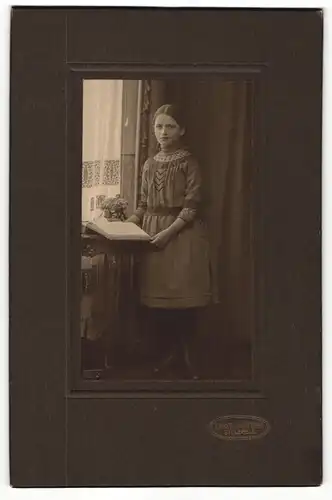 Fotografie Ernst Lohöfener, Bielefeld, Portrait modisch gekleidetes Mädchen mit Buch an Tisch gelehnt