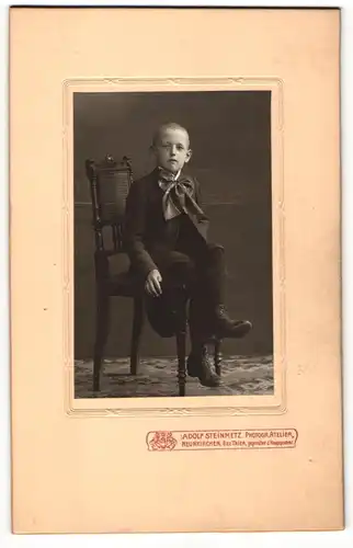 Fotografie Adolf Steinmetz, Neunkirchen Bez. Trier, kleiner auf einem Stuhl sitzender Junge im Anzug mit grosser Schleife