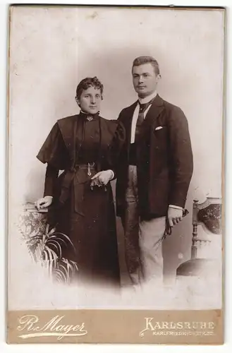 Fotografie R. Mayer, Karlsruhe, Portrait elegant gekleidetes Paar mit Buch an Tisch gelehnt