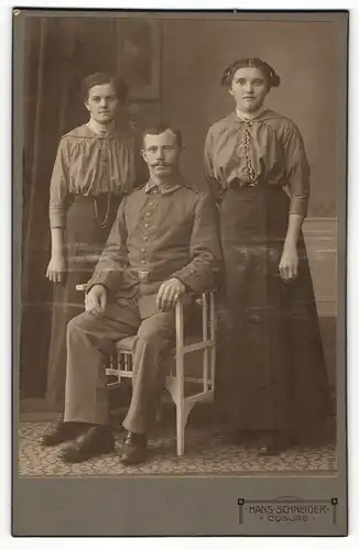 Fotografie Hans Schneider, Coburg, Portrait sitzender Soldat in Uniform und zwei bürgerliche Damen