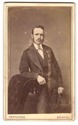 Fotografie Protheroe, Bristol, Mann im Anzug an Sessel gelehnt
