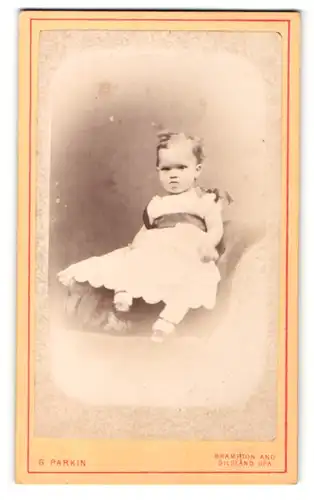 Fotografie G. Parkin, Brampton, Kleinkind im Kleidchen auf Sessel sitzend