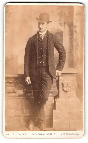 Fotografie Geo. C. Caster, Peterborough, Mann stehend im Anzug mit Hut und an Pfeiler gestützt