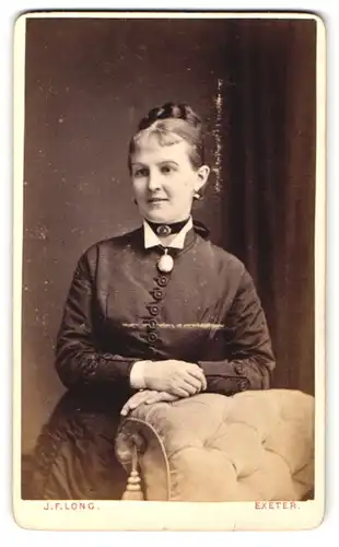 Fotografie J. F. Long, Exeter, Frau im Kleid mit Halsband und Brosche daran und Dutt