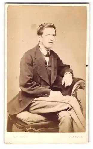 Fotografie R. Wilson, Dumfries, junger Mann sitzend auf einem Stuhl mit überschlagenen Beinen