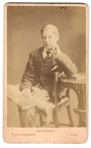 Fotografie Hills & Saunders, Eton, Junge im Anzug mit Krawatte, sitzend