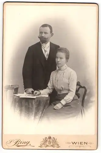 Fotografie Sigmund Bing, Wien, Portrait bürgerliches Paar in modischer Kleidung mit Bildern