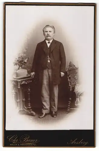 Fotografie Chr. Bauer, Arzberg, Portrait bürgerlich gekleideter Herr mit Hut an Tisch gelehnt