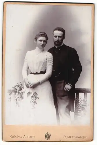 Fotografie R. Krziwanek, Ischl, Portrait elegant gekleidetes Paar mit Zweigen an Geländer gelehnt