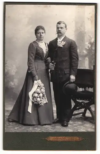 Fotografie Karl Pflanz, Linz, Portrait bürgerliches Paar in Hochzeitskleidung mit Blumenstrauss und Hut