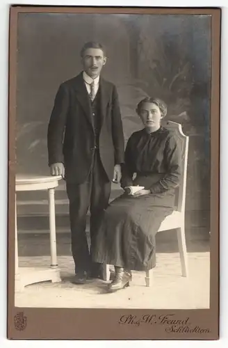 Fotografie Ph. & W. Freund, Schlüchtern, Portrait sitzende Dame in modischer Kleidung mit Heft und Herr im Anzug