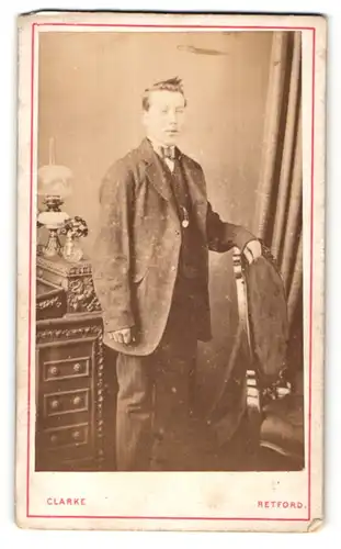 Fotografie E. Clarke, Retford, Portrait junger Herr in Anzugjacke mit Hut an Stuhl gelehnt