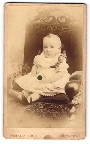 Fotografie Webster Bros, Bayswater-W, Portrait sitzendes Kleinkind im weissen Kleidchen