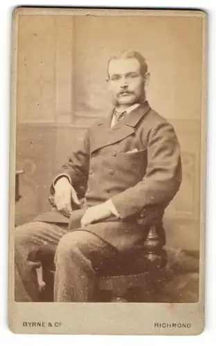 Fotografie Byrne & Co., Richmond, Portrait sitzender Herr in Anzugjacke mit Krawatte und Bart