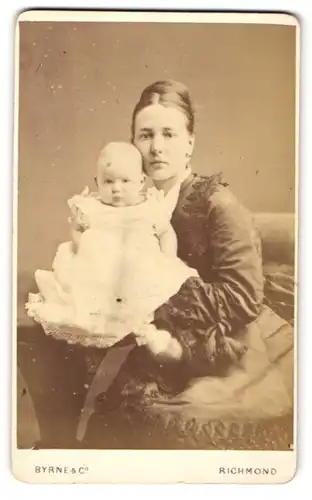 Fotografie Byrne & Co, Richmond, Portrait schöne junge Mutter mit süssem Baby im Taufkleidchen