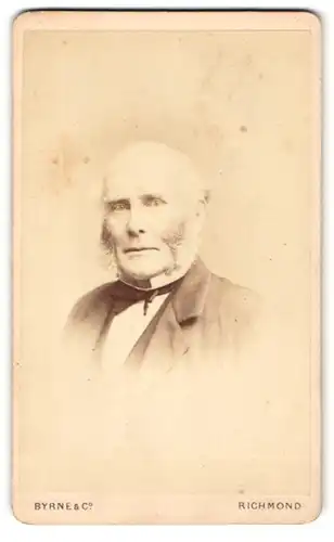 Fotografie Byrne & Co, Richmond, Portrait betagter Herr mit Kotelettenbart und Fliege im Jackett