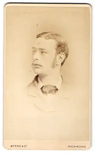 Fotografie Byrne & Co, Richmond, Portrait lässiger junger Mann mit Scheitel und Fliege im Jackett