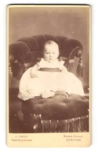 Fotografie J. & E. Owen, Newtown, Baby im weissen Kleid sitzend in einem Stuhl