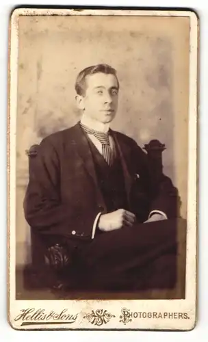 Fotografie Hellis & Sons, London, Portrait sitzender charmanter Herr im Anzug mit Krawatte