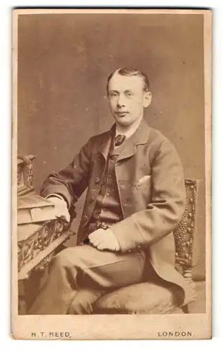 Fotografie H. T. Reed, London, Portrait elegant gekleideter Herr am Schreibtisch sitzend