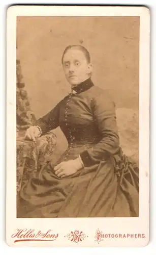 Fotografie Hellis & Sons, London, Portrait sitzende Dame im eleganten Kleid mit Kragenbrosche