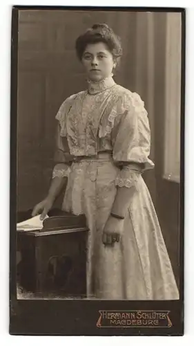 Fotografie Hermann Schlüter, Magdeburg, Portrait hübsch gekleidete Dame mit Zeitung an Tisch gelehnt
