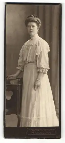 Fotografie Hermann Schlüter, Magdeburg, Portrait hübsch gekleidete Dame mit Buch an Kommode gelehnt