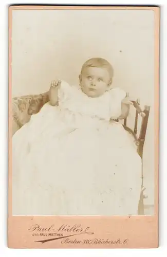 Fotografie Paul MÜller, Berlin-SW, Portrait sitzendes Kleinkind im weissen Kleid mit kurzen Haaren