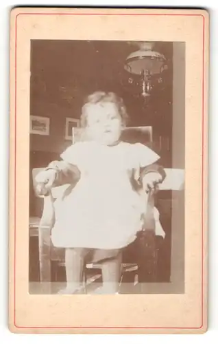 Fotografie unbekannter Fotograf und Ort, kleines auf dem Stuhl sitzendes Mädchen im hellen Kleid