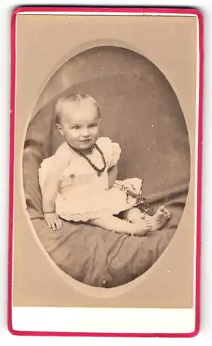 Fotografie unbekannter Fotograf und Ort, Portrait sitzendes Kleinkind im weissen Kleid mit Halskette