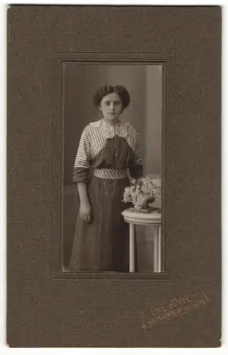 Fotografie Emil Hoppe, Hartmannsdorf, Portrait modisch gekleidete Dame mit Blumen an Tisch gelehnt